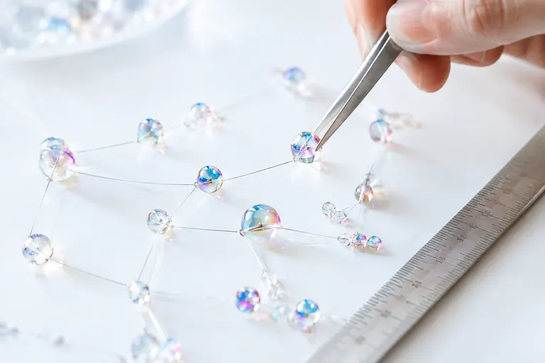 Main posant une perle de verre dans une constellation reliée par des fils argentés